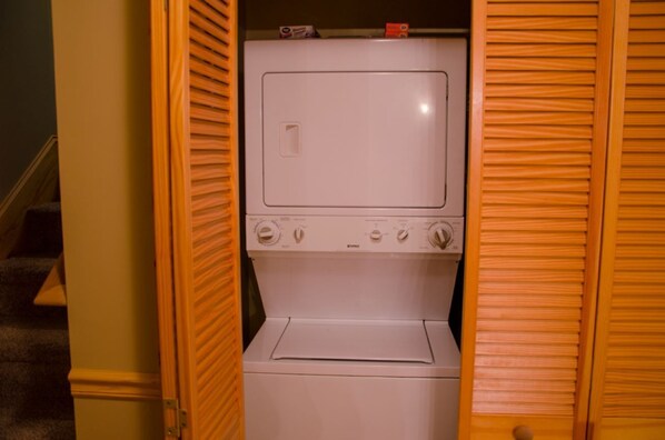 A white washer and dryer unit in a wooden closet with a door.