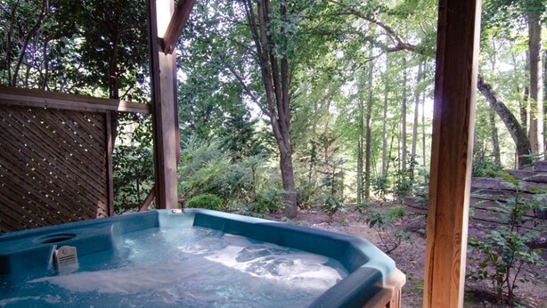A hot tub in a wooded area with a wooden deck and a lattice fence.