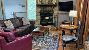 A cozy living room with a stone fireplace, a red sofa, a striped chair, and a television mounted on the wall.