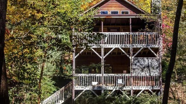 A wooden cabin with a balcony, surrounded by trees.