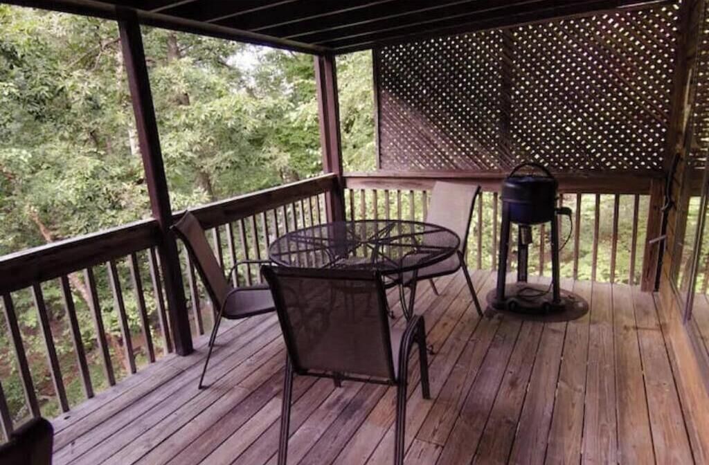 A covered outdoor area with a wooden deck, a round table with chairs, and a grill.