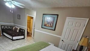 A bedroom with a bed, a ceiling fan, a door, and a painting on the wall.