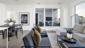 A modern living room with a sofa, a dining table, and a large window offering a city view.