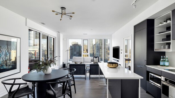 A modern kitchen with a central island, black and white cabinetry, and a view of the cityscape through large windows.