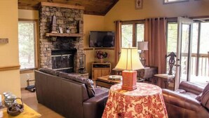 A cozy living room with a stone fireplace, leather sofas, a television, and a table with a lamp.