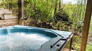 A hot tub in a natural setting with wooden decking and lush greenery in the background.