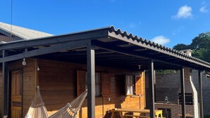 Une cabane en bois dotée d’une terrasse couverte, d’un hamac, d’une table de pique-nique et d’un four en briques.