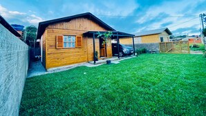 Une maison en bois avec un abri pour voiture, une cour clôturée et un ciel dégagé.