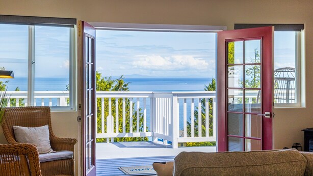 Ein Zimmer mit Meerblick, ein Korbstuhl, eine rote Tür und ein weißes Geländer auf dem Balkon.