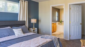 Ein Schlafzimmer mit Bett, Nachttisch, Lampe und Blick ins Badezimmer.