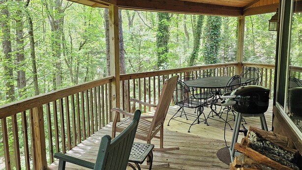 A wooden deck with a ceiling fan, outdoor seating, and a view of a forest.