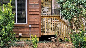 A rustic cabin with a stone wall, wooden deck, and a sign reading "DON'S DEN 10".