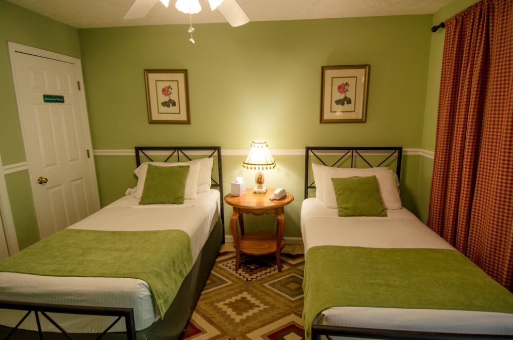 Et værelse med to senge, et lille bord med en lampe, og en dør med teksten 'Master Bedroom'.