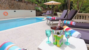 A poolside area with lounge chairs, a table with drinks, and a stone wall. - 5 Bedroom, luxury private villa with pool & 360' ocean views (Gros Islet)