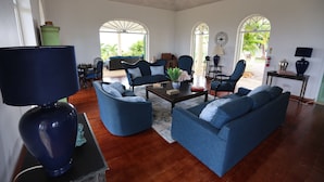 A spacious living room with a blue sofa set, a coffee table, and a lamp. There are two chairs, a small table, and a decorative vase. - 5 Bedroom, luxury private villa with pool & 360' ocean views (Gros Islet)