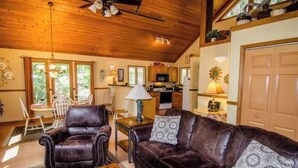 A cozy living room with a leather sofa, a dining area with a table and chairs, and a kitchen in the background. - Your PGA TOUR Basecamp in the Blue Ridge Mountains (Asheville)