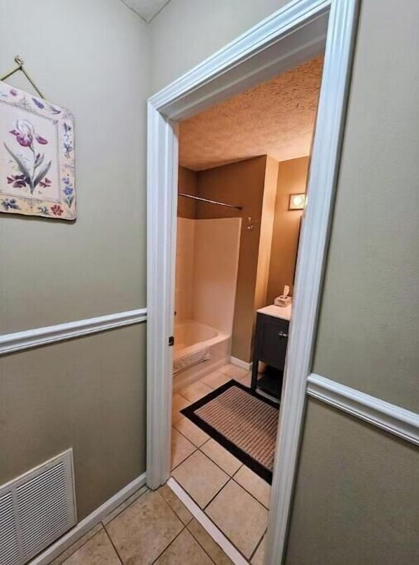 A narrow hallway with a door leading to a bathroom. The bathroom has a bathtub, a shower, and a small cabinet.