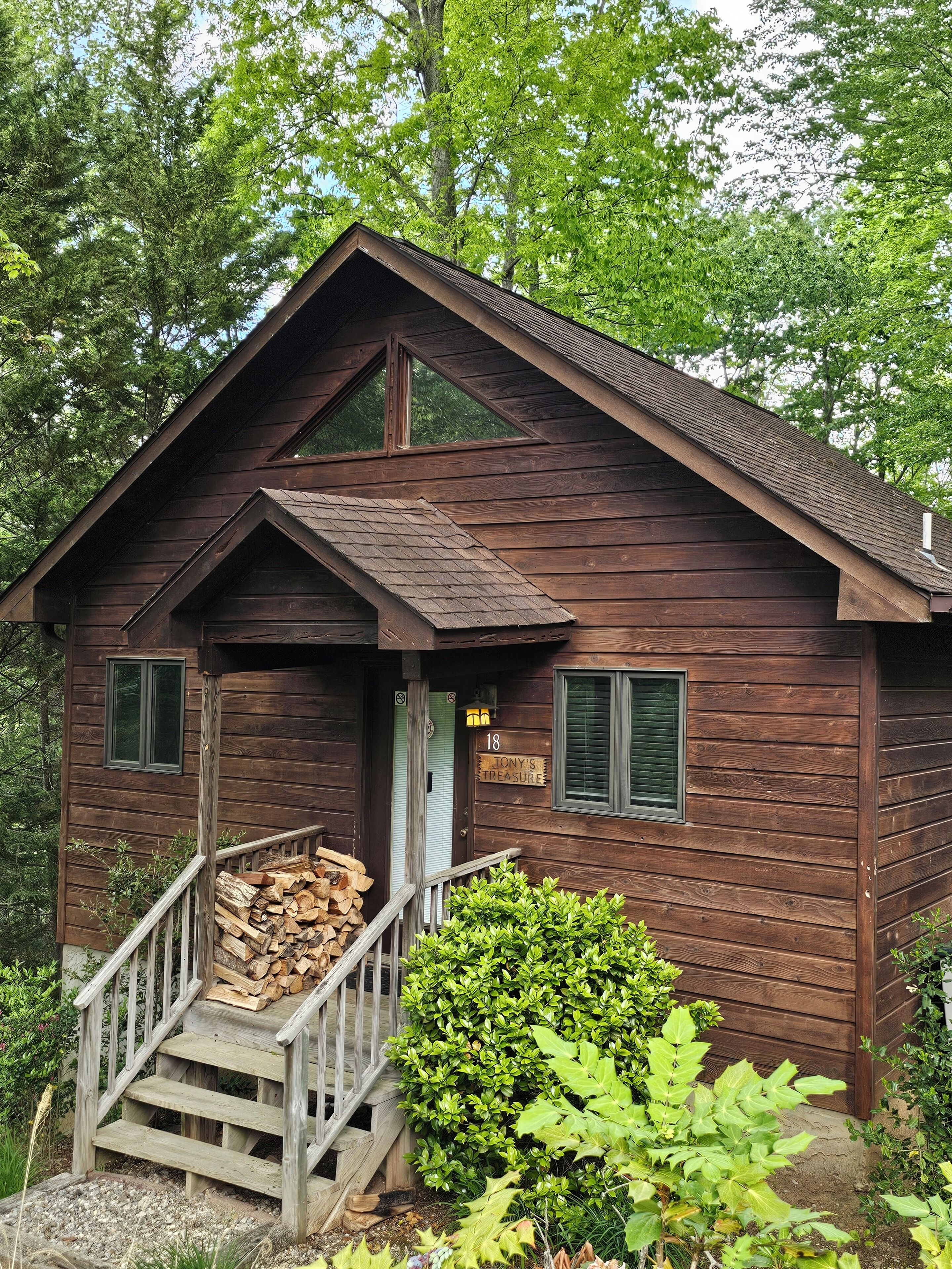A wooden cabin with a porch, a number sign, and a stack of firewood.