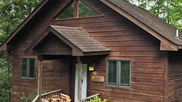A wooden cabin with a porch, a number sign, and a stack of firewood.