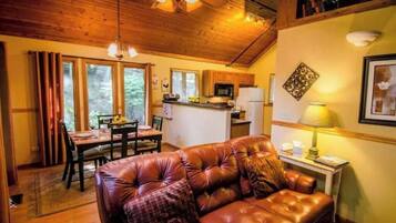 A cozy living room with a leather sofa, wooden ceiling, and a dining area with a table and chairs.