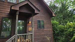 A two-story wooden cabin with a porch, a sign reading "JESSIE MAGNUS," and a number "19." - Stay Near Asheville's PGA TOUR – Hot Tub & Access to the Mtn to Sea Trail (Asheville)
