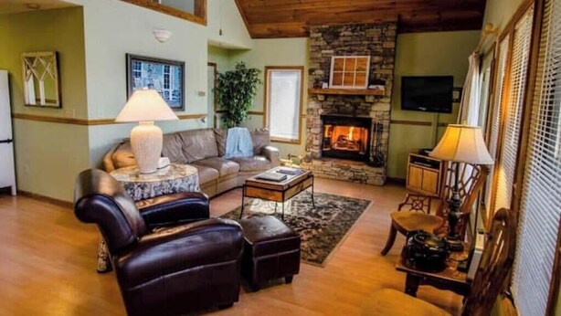 A cozy living room with a stone fireplace, leather sofas, and a television. - Stay Near Asheville's PGA TOUR – Hot Tub & Access to the Mtn to Sea Trail (Asheville)