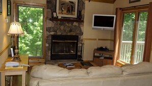 A cozy living room with a stone fireplace, a television mounted above it, and a comfortable sofa. - Perfect Honeymoon cabin w/hot tub (Asheville)