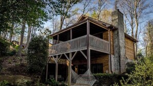 A wooden cabin with a balcony, surrounded by trees and a hammock. - Romantic getaway w/hot tub (Asheville)