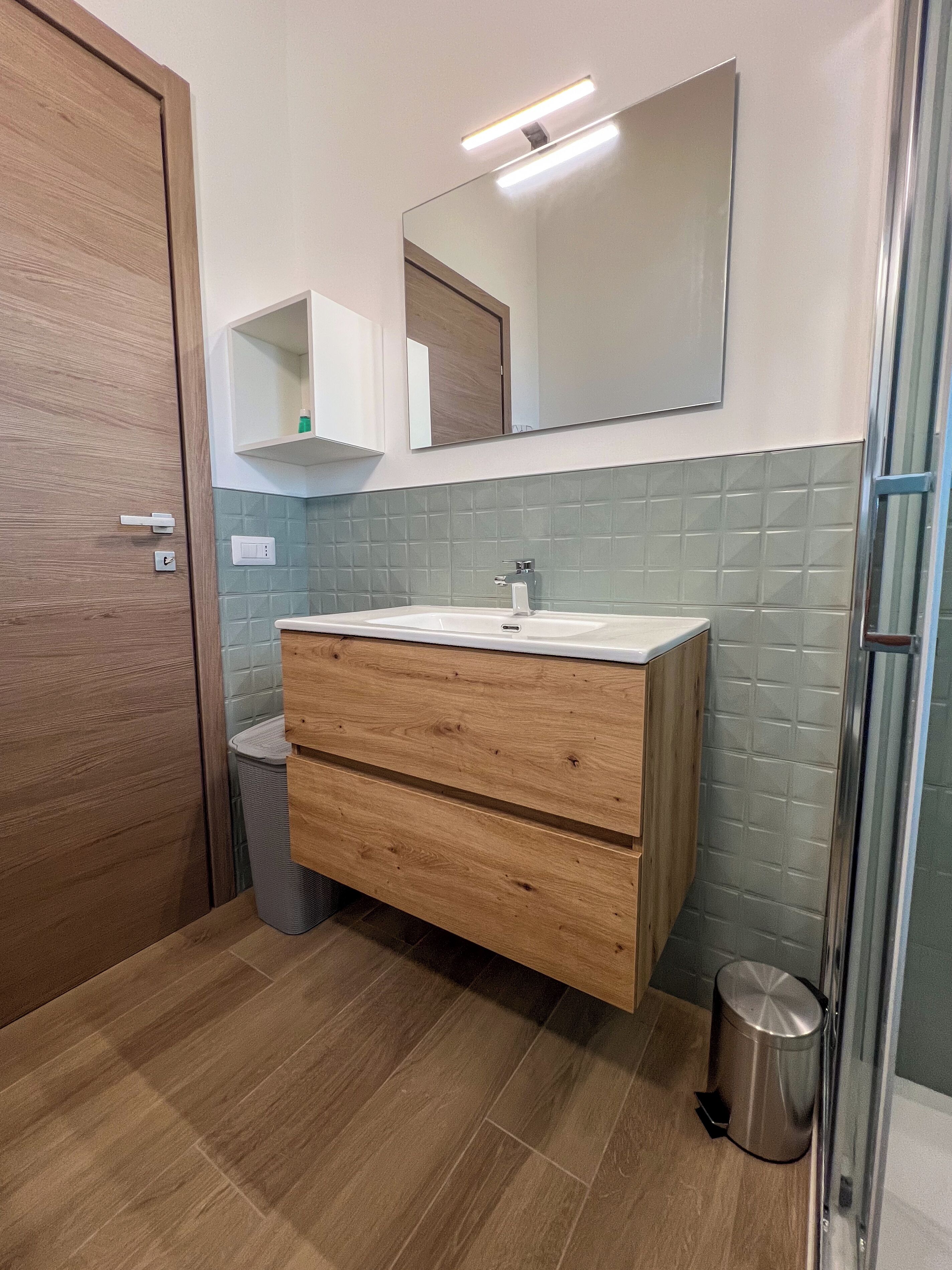 Ein modernes Badezimmer mit einem Holzbadezimmer-Möbel, einem Spiegel und einer gefliesten Rückwand.