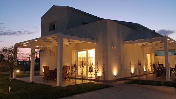 A modern house with a covered patio, a dining area, and a well-lit interior. - Villa Green - Zannafondo Villas with private garden and 100 mt from the beach (Kaukana)