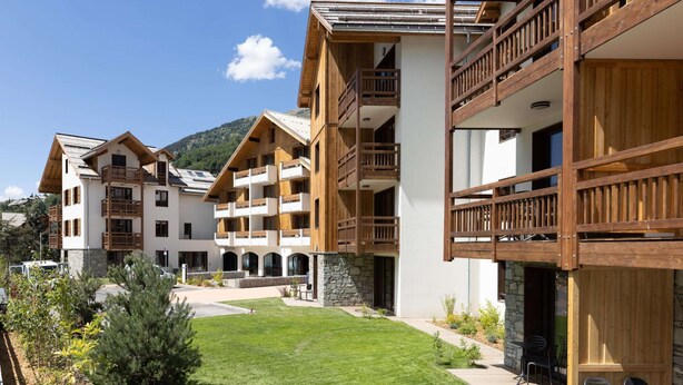 Un hôtel à plusieurs étages doté de balcons en bois, d’une cour avec une pelouse et de murs en pierre.