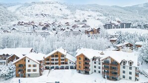 Une station de ski enneigée, avec plusieurs bâtiments en bois, dont un grand chalet doté de balcons, et un télésiège visible au loin.