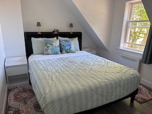 Un dormitorio con cama, mesitas de noche, ventana y radiador.