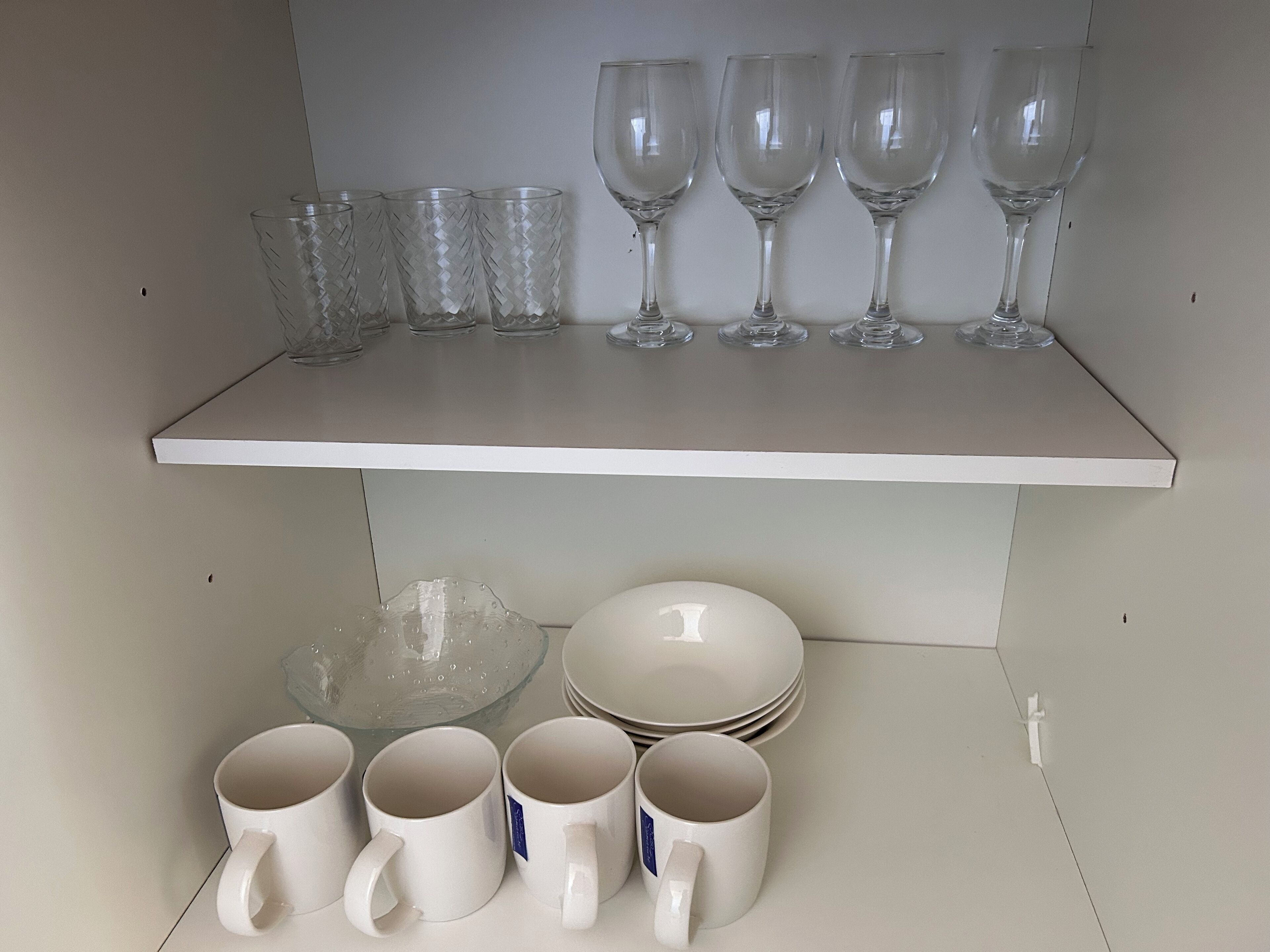 A shelf with clear glassware and white mugs.