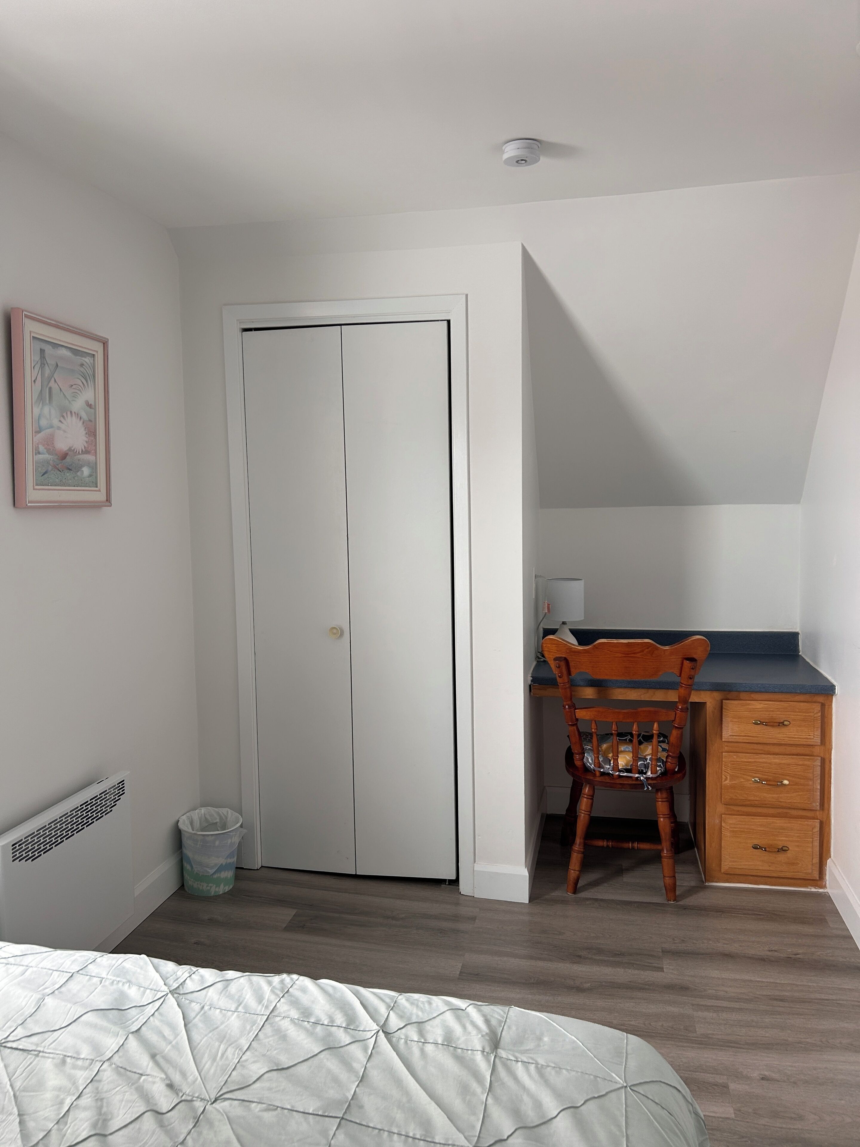 A bedroom with a bed, a desk, a chair, a radiator, and a door.