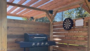 An outdoor wooden deck with a grill, a propane tank, and a dartboard labeled 'Garden View.'