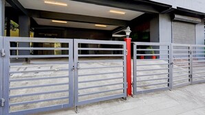 Een omheind toegangspunt naar een gebouw met een metalen poort en een rode pilaar.