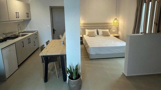 A modern apartment with a kitchen, dining area, and a bedroom with a bed and bedside table. - KYNTHIA seaview apartments (Samos)