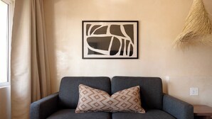 Un canapé gris agrémenté d’un coussin à motifs, une œuvre d’art abstraite encadrée accrochée au mur et une plante suspendue.