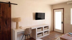Une chambre à coucher avec un lit, un bureau avec une chaise, une télévision et une porte.