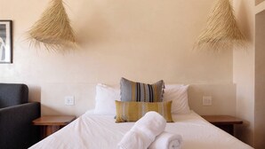 Une chambre d’hôtel comprenant un lit, deux tables de chevet, une chaise et deux lampes suspendues.