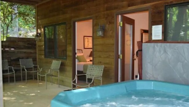 A wooden cabin with a hot tub, outdoor seating, and a door leading to a bedroom.