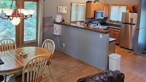 A kitchen with wooden cabinets, a stainless steel refrigerator, and a dining area with a wooden table and chairs.