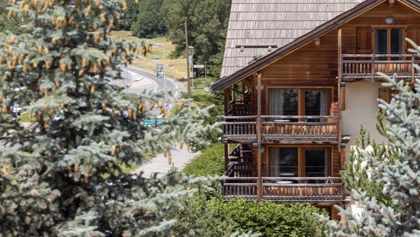 A wooden chalet with a balcony, surrounded by trees and mountains in the background. - Apartment in Chantemerle Near Ski Slopes (Saint-Chaffrey)