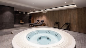 A modern spa area with a central hot tub, lounge chairs, and a seating area with a wooden bench. - Apartment in Chantemerle Near Ski Slopes (Saint-Chaffrey)