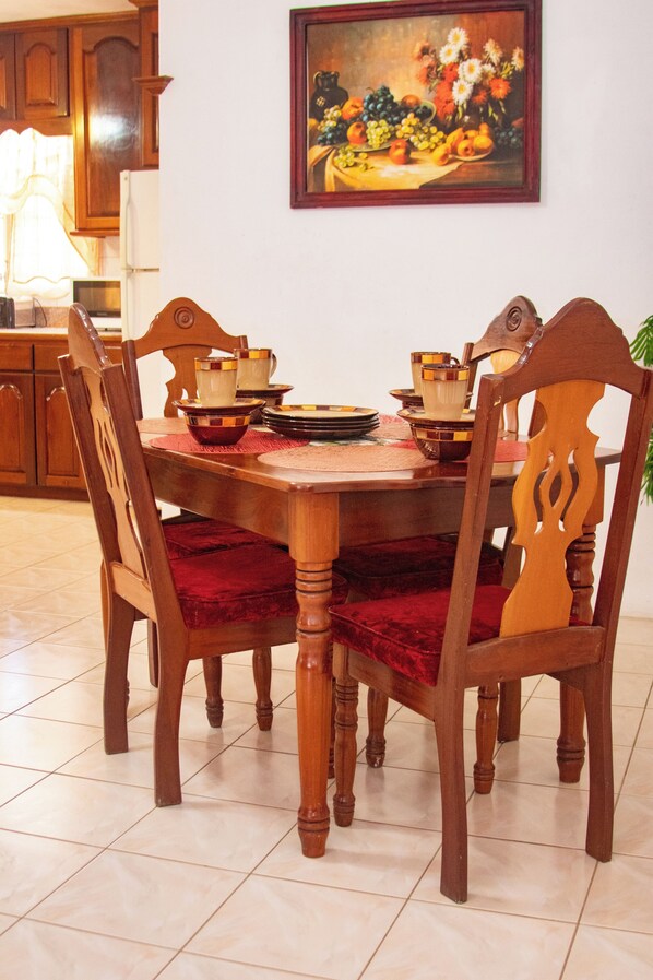 Una mesa de comedor con sillas, un cuadro en la pared y una zona de cocina al fondo.