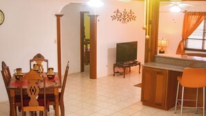 A dining area with a wooden table and chairs, a television, and a kitchen counter. - 2-Bedroom/Bath Comfortable AI Residence- 
A/C, WiFi and 7 mins away from beach. (Statia Valley)