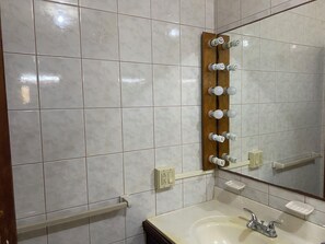 Un baño con azulejos blancos, un perchero de madera, un espejo, un lavamanos y un grifo.