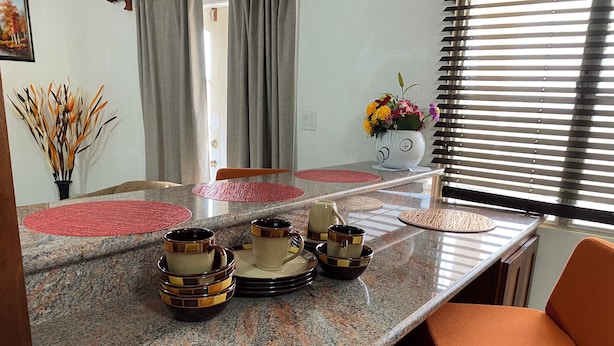 A dining area with a granite countertop, matching plates, and a vase of flowers. - 2-Bedroom/Bath Comfortable AI Residence- 
A/C, WiFi and 7 mins away from beach. (Statia Valley)