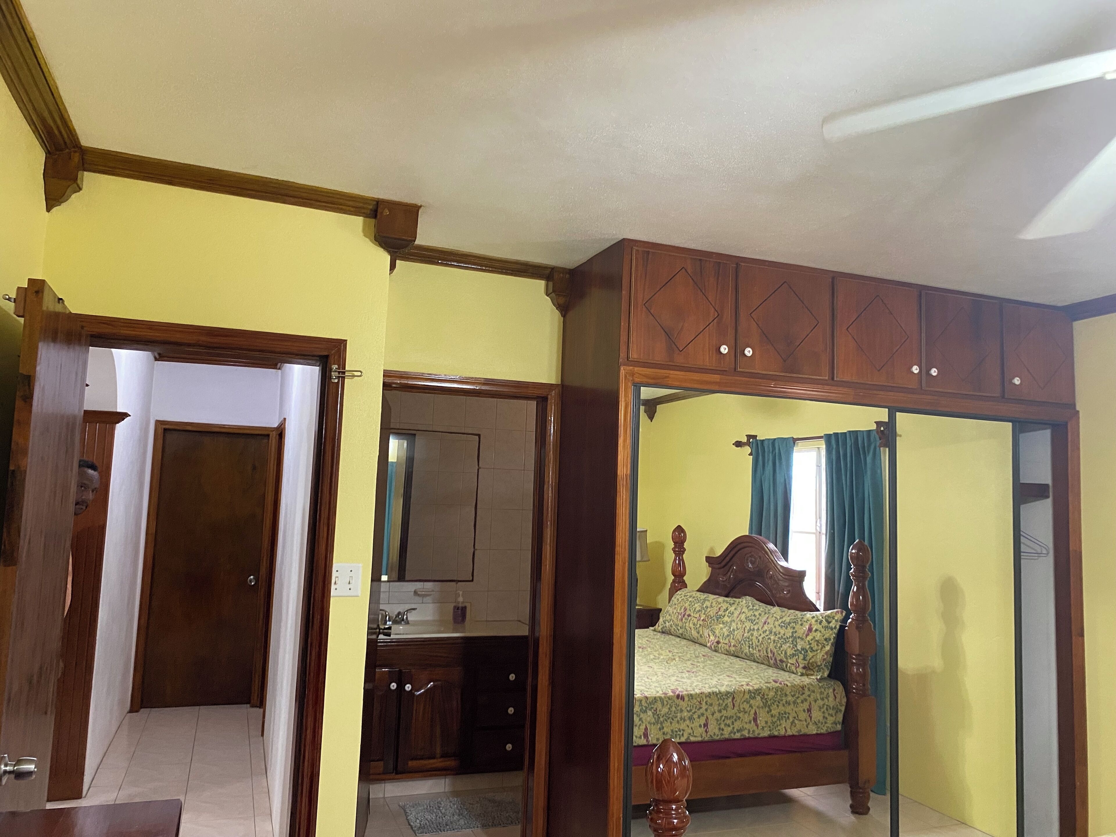 Une chambre à coucher avec un lit, une armoire en bois et une salle de bain visible à travers une porte ouverte.